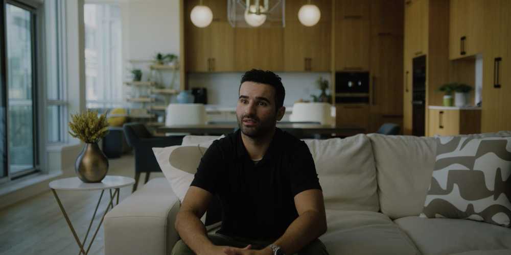 a man sitting on a white couch with a kitchen in the background