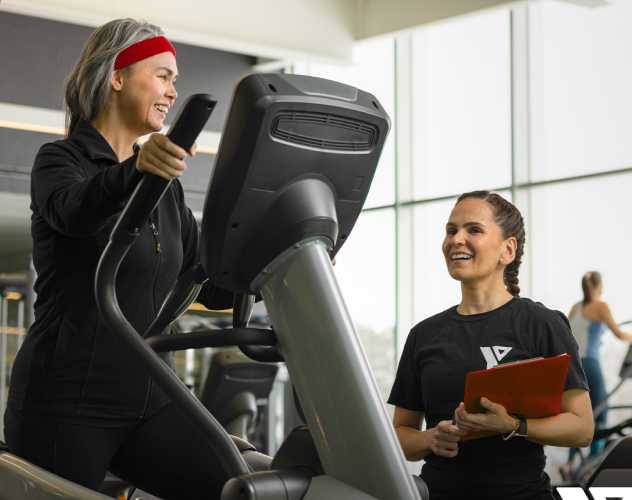 a older woman on an elliptical talking to an employee of the YMCA