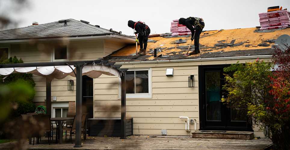 two employees of AMGROUP Exteriors removing shingles off a roof
